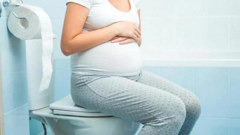 임산부가 변비 때문에 화장실 변기에 앉아서 배를 만지고 있는 모습