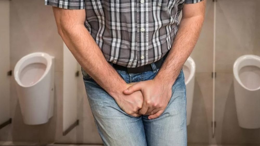 한 남성이 남자 화장실에서 양손을 중심 부위에 모으고 소변을 참고 있는 듯한 모습