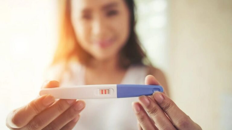 한 여성이 양성이 나온 임신테스트기를 양 손으로 들고 있는 모습