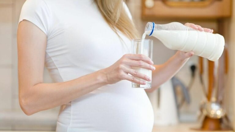 임신부가 한손에 우유통을 들고 다른 한손에 있는 유리컵에 우유를 따르고 있는 모습