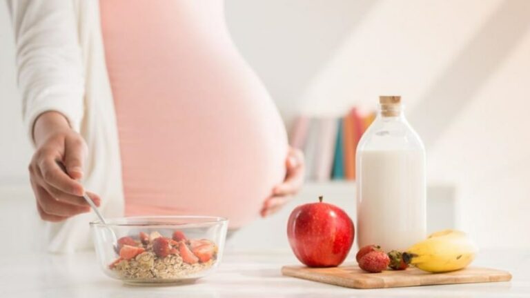 임신부가 우유와 사과 등이 놓여진 식탁 옆에 서 있는 모습