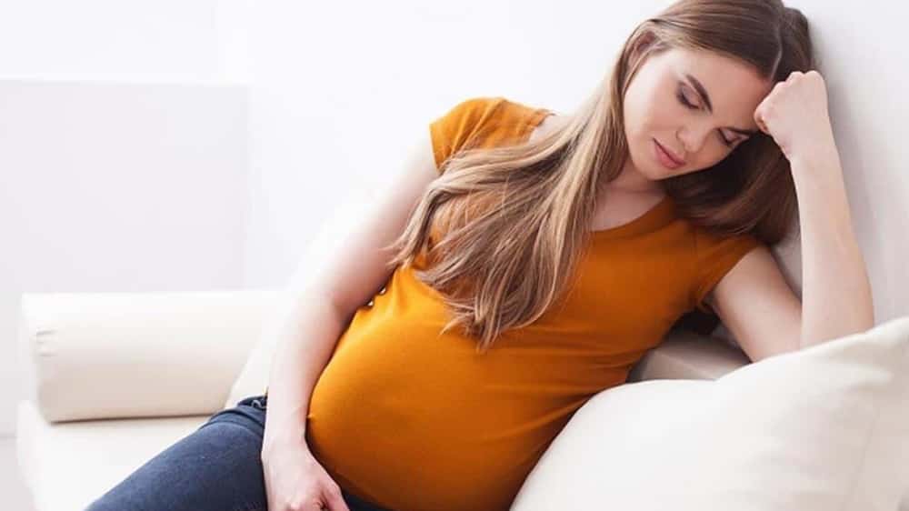임신부가 소파에 기대 앉아 머리를 주먹으로 누르고 있는 이미지