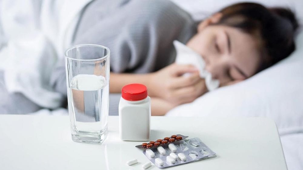 인플루엔자 바이러스 독감 관련 침대에 한 여자가 휴지로 코를 풀면서 누워 있고 그 앞에 약과 물이 놓여 있는 이미지