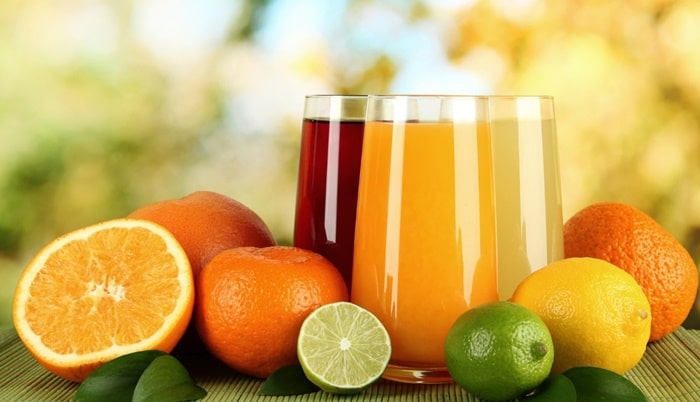 유리잔 안에 노란색과 빨간색 과일 주스가 담겨져 있고 그 옆에 오렌지와 라임 등의 과일이 함께 놓여진 모습