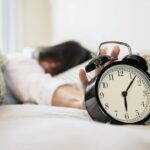 잠을 충분히 못 잤을 때 나타나는 증상 관련 침대에 엎드려서 자명종 시계에 손을 갖다 대고 끄려고 하는 모습