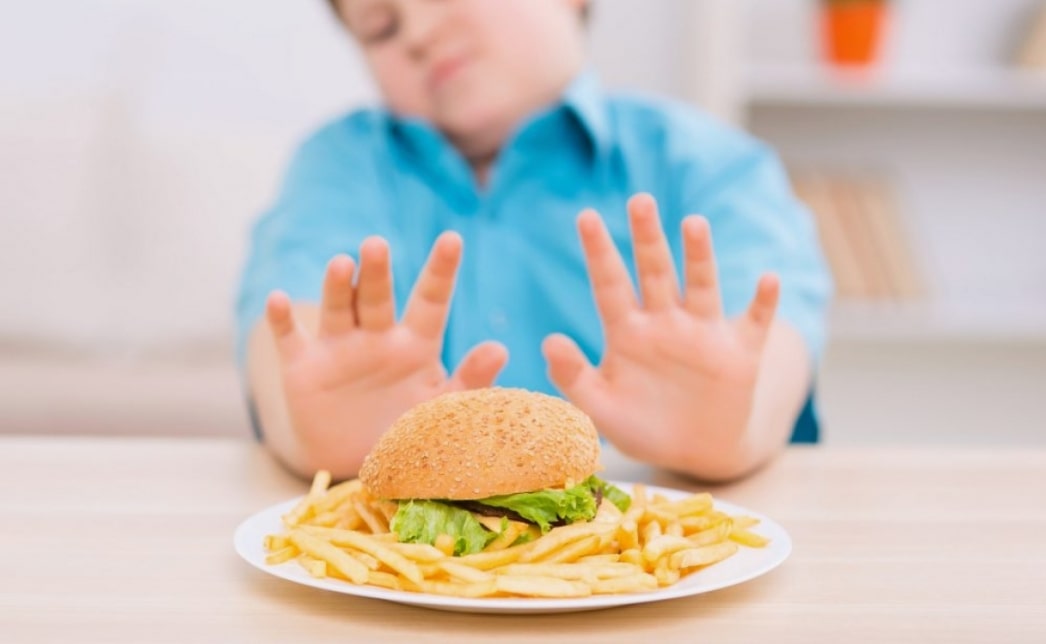 소아비만 예방 관련 아이가 핸버거와 감자튀김이 든 접시를 양 손으로 밀어내는 모습