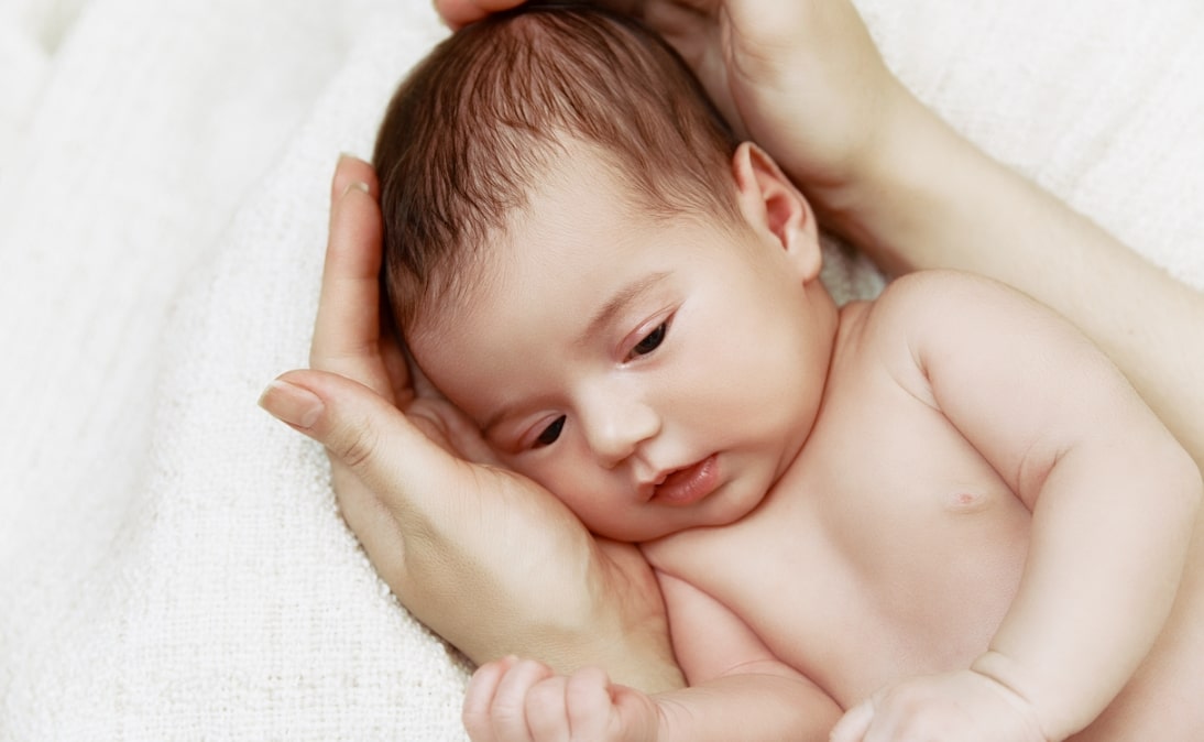 신생아가 누워 있고 양 손으로 신생아의 목과 몸을 받치고 있는 모습
