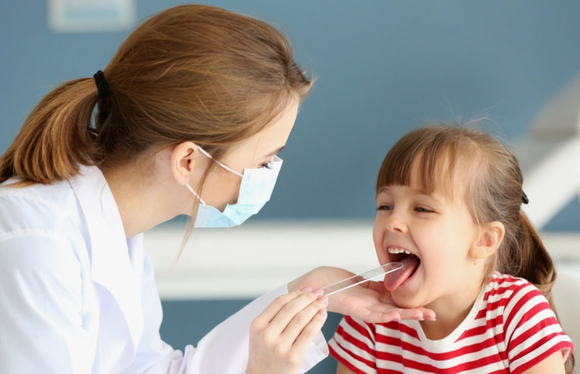 의사가 아이의 혀를 기구로 누르고 진찰하는 모습