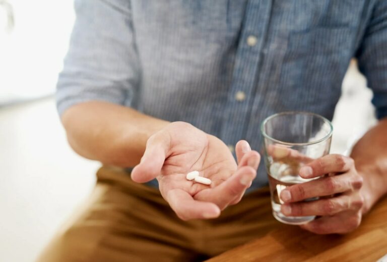 남성이 앉아서 한 손에 약을 들고 있고 다른 손에 물컵을 들고 있는 모습